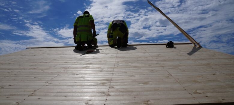 Kaksi rakennusmiestä kunnostamassa laavun kattoa
