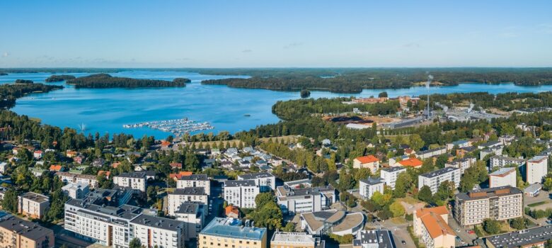 Ilmakuva kesäisestä kaupungista, jossa näkyy Lohjan keskusta, asuinrakennuksia, venesatama ja järvimaisema taustalla.